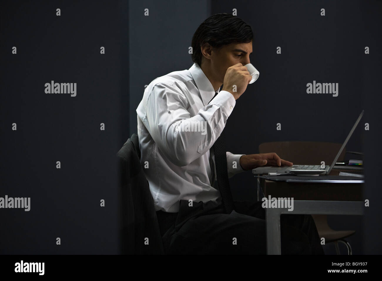 Uomo in ufficio a bere caffè, lavora fino a tardi Foto Stock