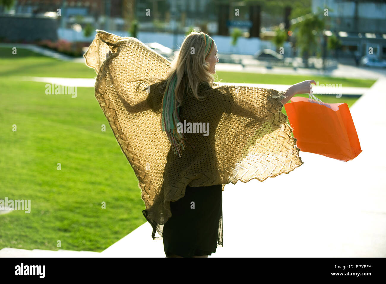 Donna che indossa scialle, passeggiate nel parco con le braccia aperte, shopping bag in mano Foto Stock