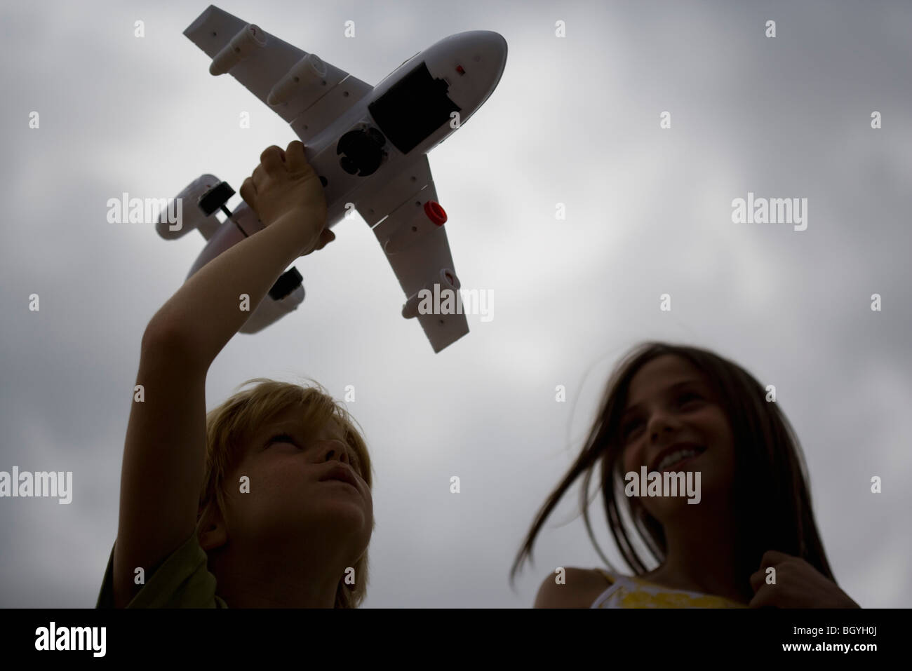 Ragazzo giocando con aeroplano giocattolo, sorella guardando, sorridente Foto Stock