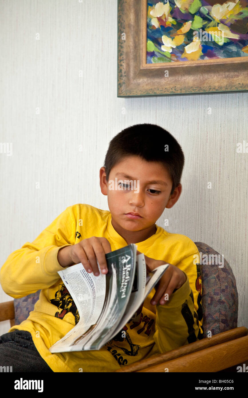 Bambini rivista di lettura 8-10 anni ragazzo ispanico attesa per il suo appuntamento con il medico. Stati Uniti signor © Myrleen Pearson Foto Stock