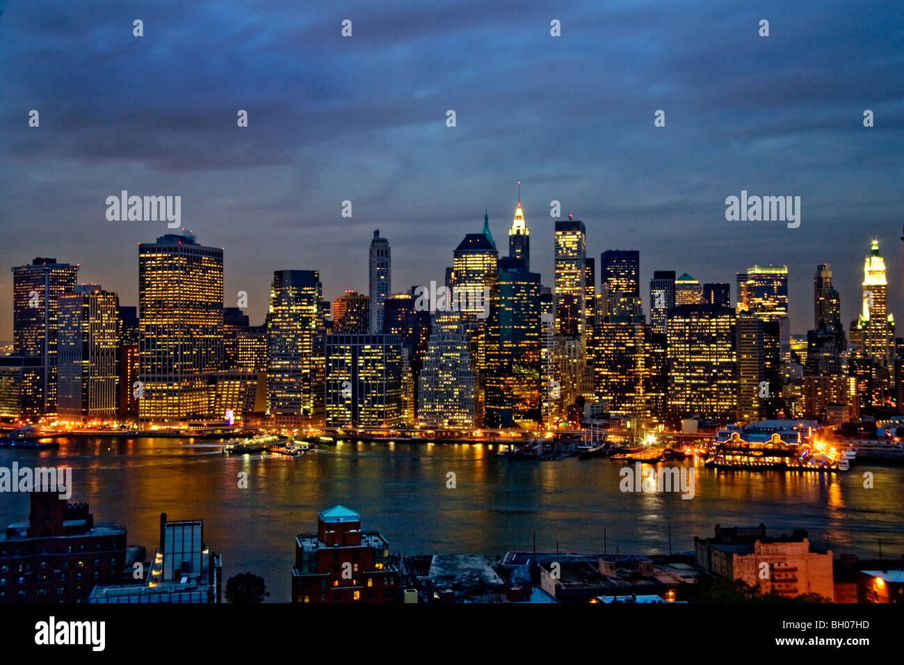 Le luci di Lower Manhattan, NY City, scintillano al crepuscolo in tutta l'East River. Questa parte della città è la casa di Wall Street Foto Stock