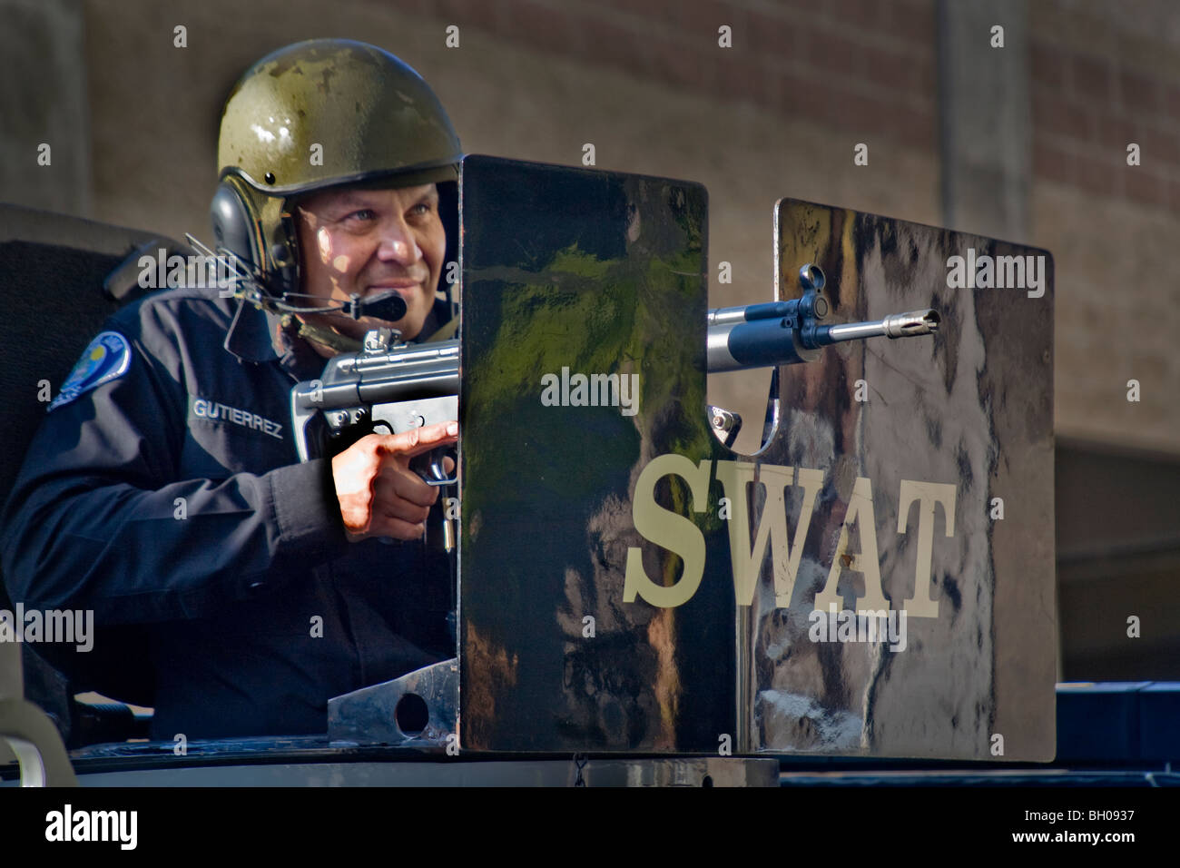 Indossa un casco in acciaio, un ispanico SWAT (Armi speciali e operazioni tattiche) del team ufficiale di polizia mira una mitragliatrice nota scudo corazzato Foto Stock