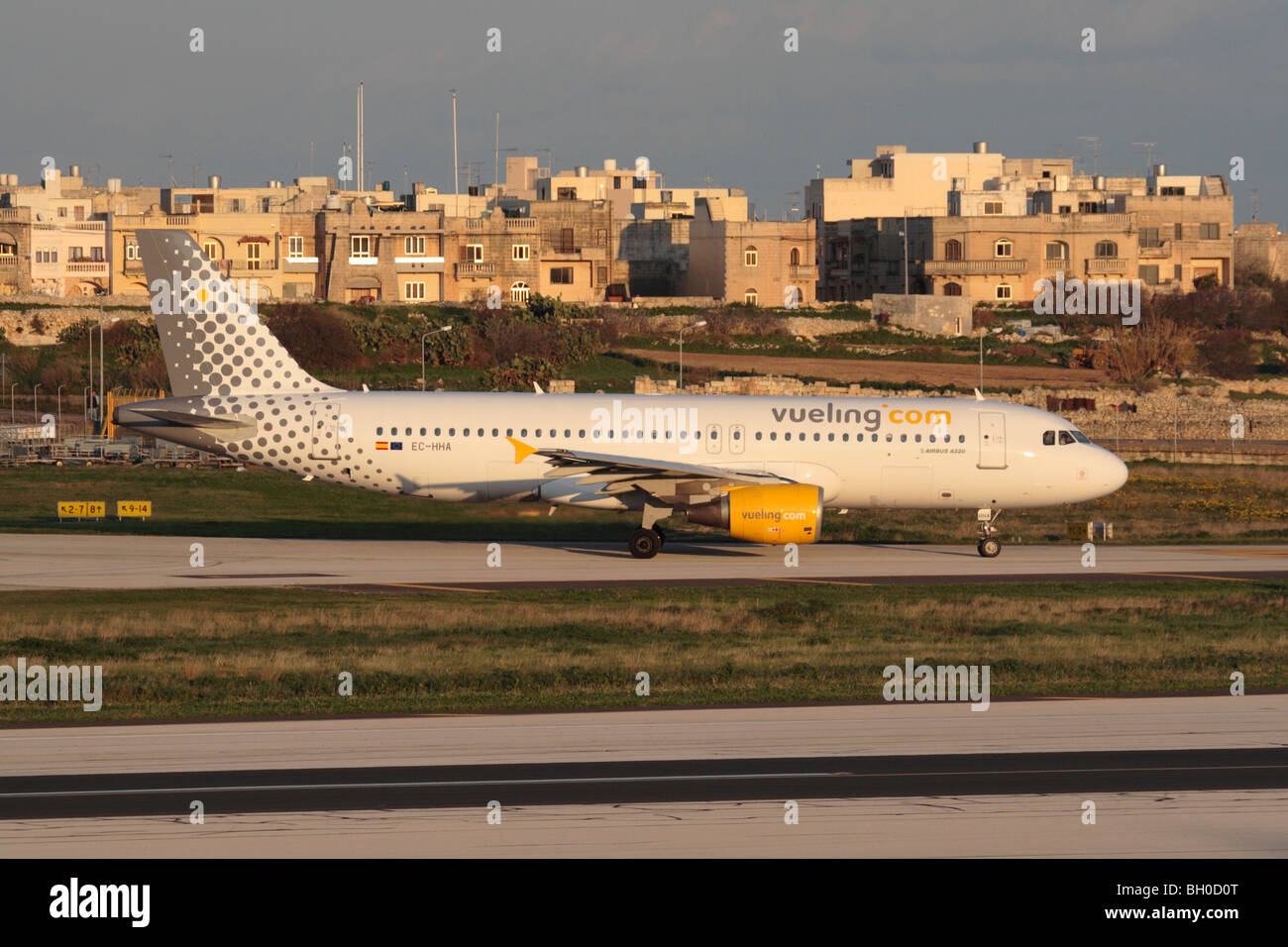 Basso costo viaggi aerei e il turismo di massa. Vueling Airbus A320 di rullaggio per la partenza da Malta al tramonto Foto Stock