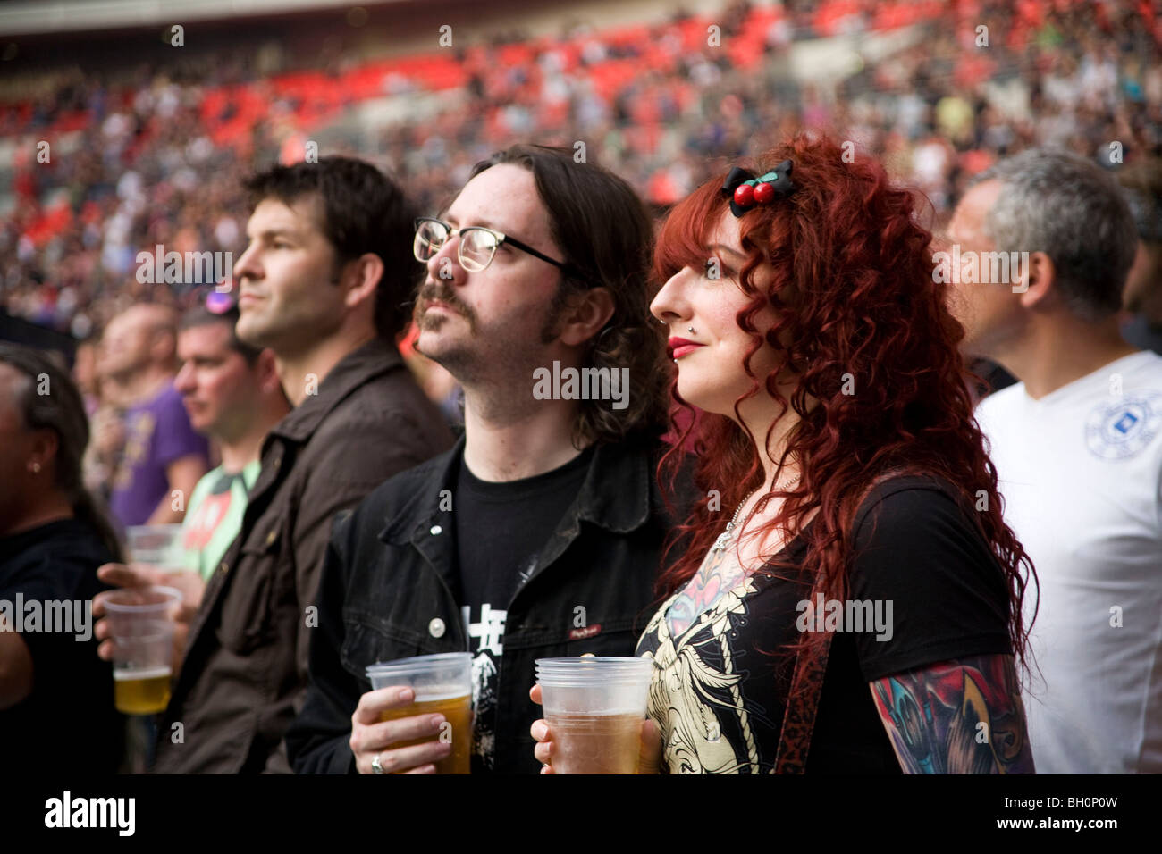 Tatuato ventola femmina con partner barbuto la visione di concerto e di bere birra, AC/DC a Wembley Stadium, Giugno 2009 Foto Stock