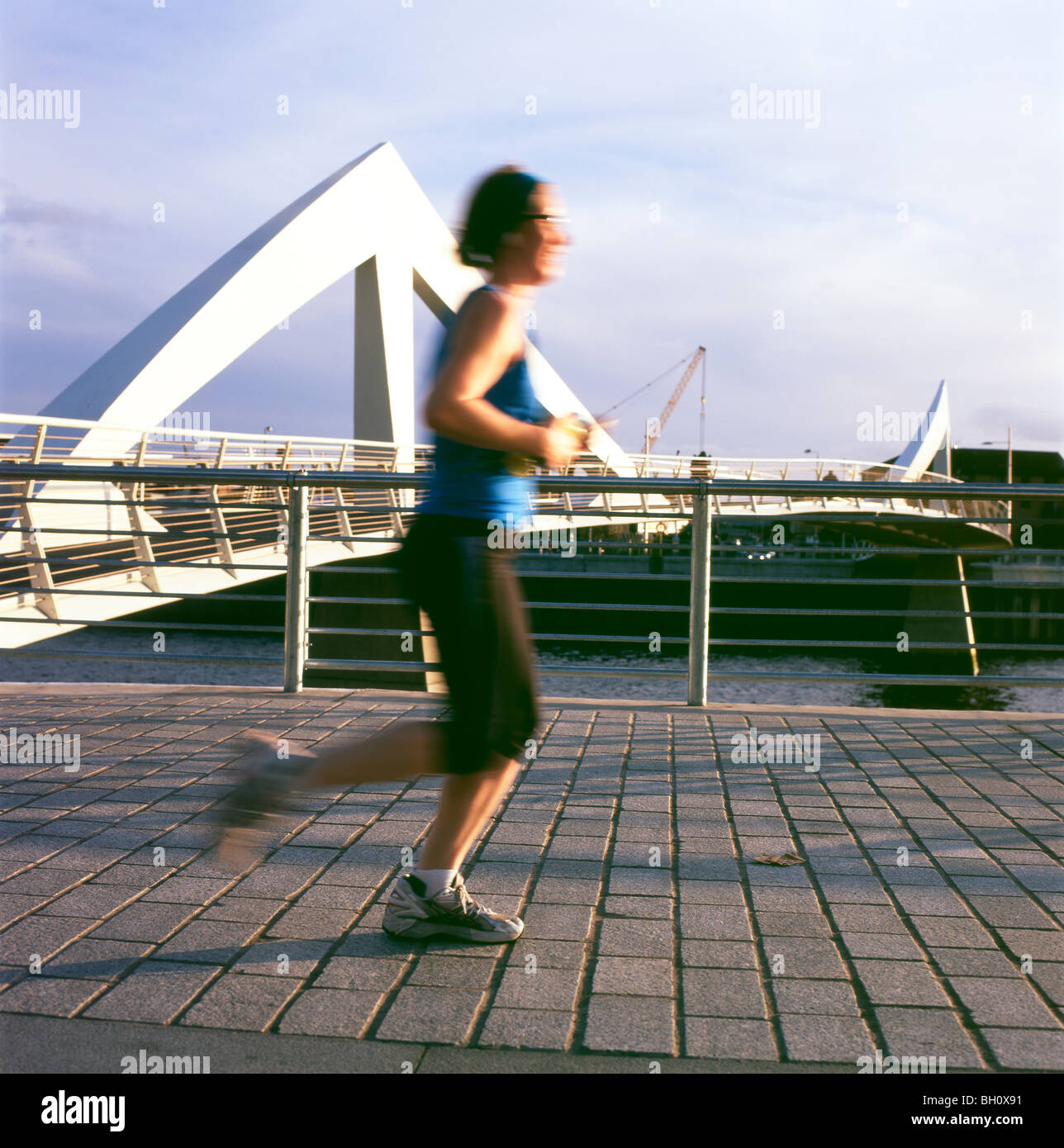 Giovane donna runner jogger su jogging jogging lungo il fiume Clyde passando per il ponte Tradeston a Glasgow Scozia Regno Unito KATHY DEWITT Foto Stock