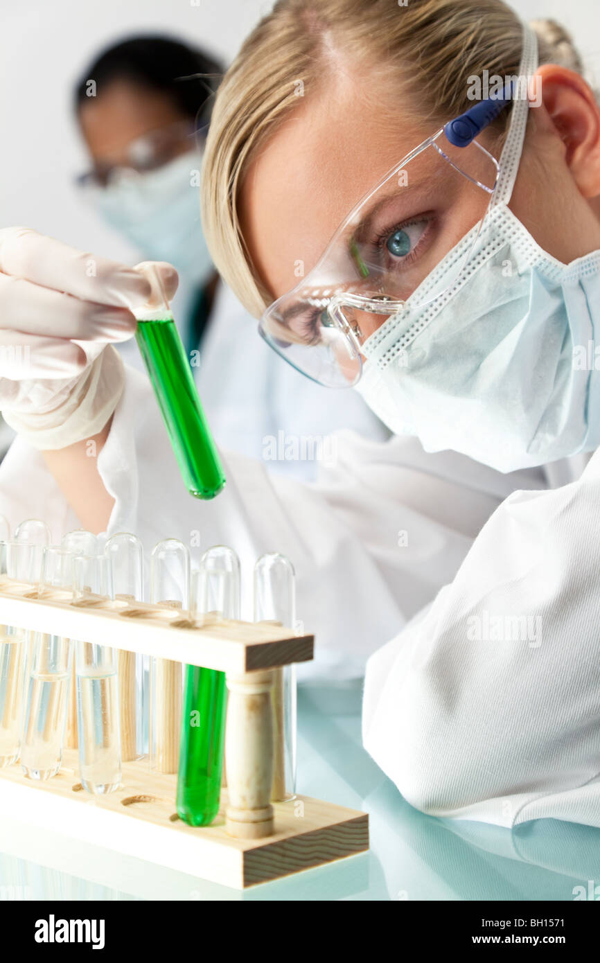Una bionda medico o ricercatore scientifico o medico guardando un tubo di prova della soluzione di verde in un laboratorio. Foto Stock