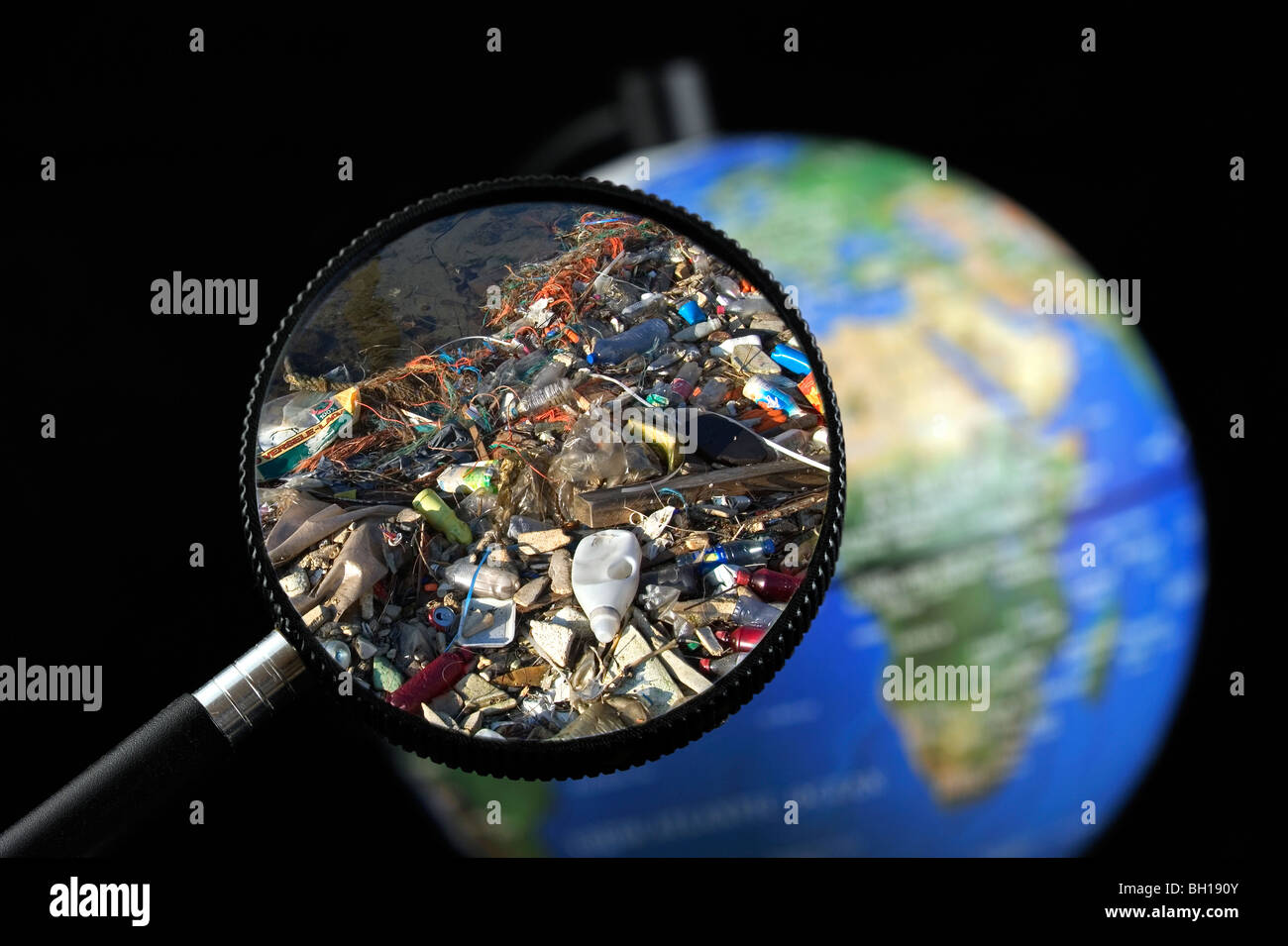 Rifiuti non degradabile / rifiutare in acqua si è incagliata vista attraverso la lente di ingrandimento tenuto contro illuminato globo terrestre Foto Stock