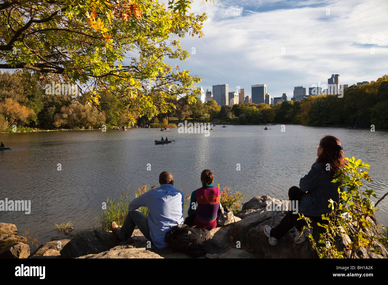 La gente guarda i barcaioli del Lago di Central Park in una giornata di caduta con lo skyline di Manhattan in distanza. Foto Stock