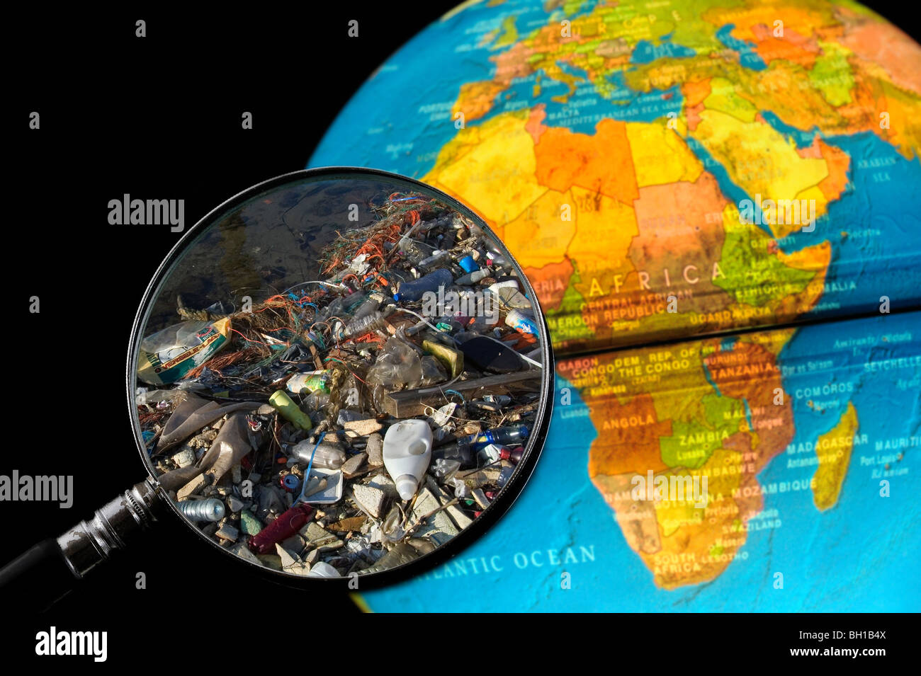 Rifiuti non degradabile / rifiutare in acqua si è incagliata vista attraverso la lente di ingrandimento tenuto contro illuminato globo terrestre Foto Stock