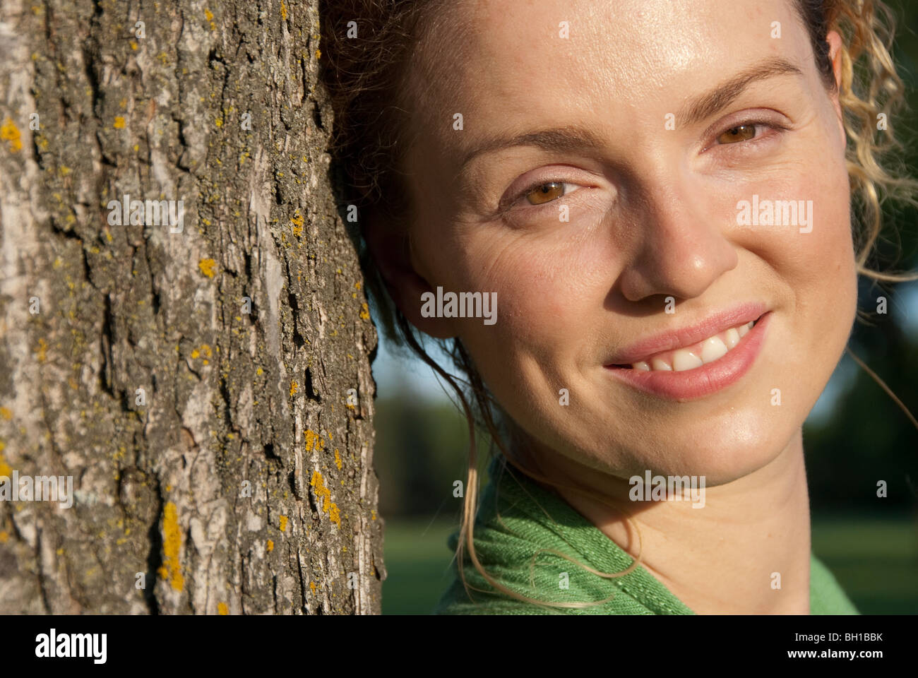 Colpo alla testa della donna nella sua 40s accanto all albero, Assiniboine Park, Winnipeg, Manitoba, Canada Foto Stock