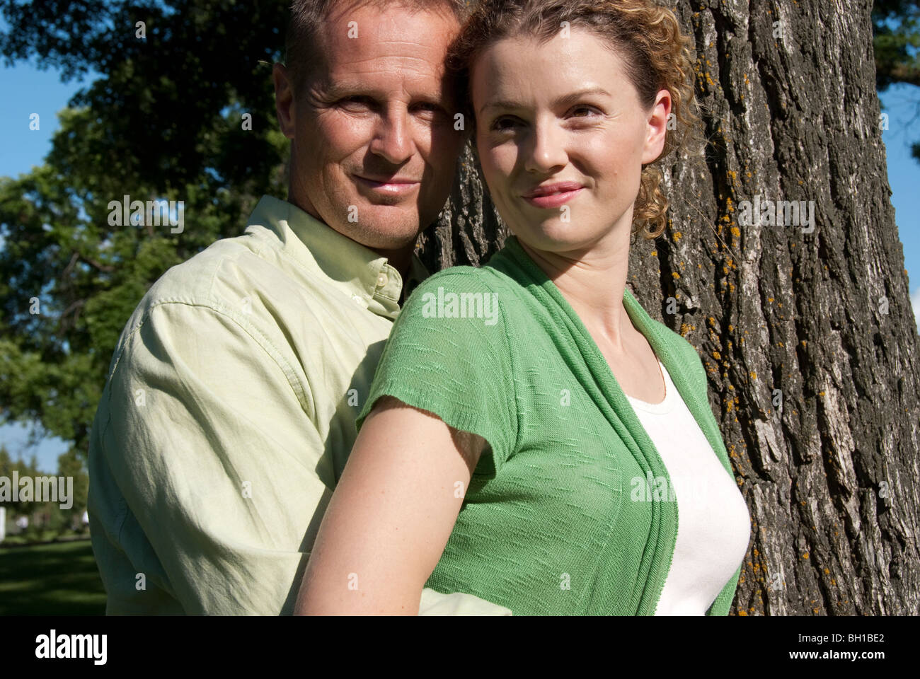 Matura nel loro 40s abbracciare accanto all albero in Assiniboine Park, Winnipeg, Manitoba, Canada Foto Stock