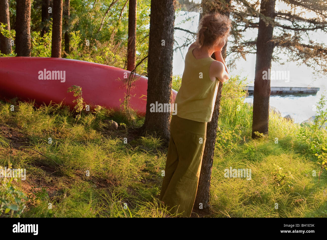 Donna appoggiata contro la struttura si affaccia sul lago, Clear Lake, equitazione di montagna del Parco Nazionale, Maniotba, Canada Foto Stock