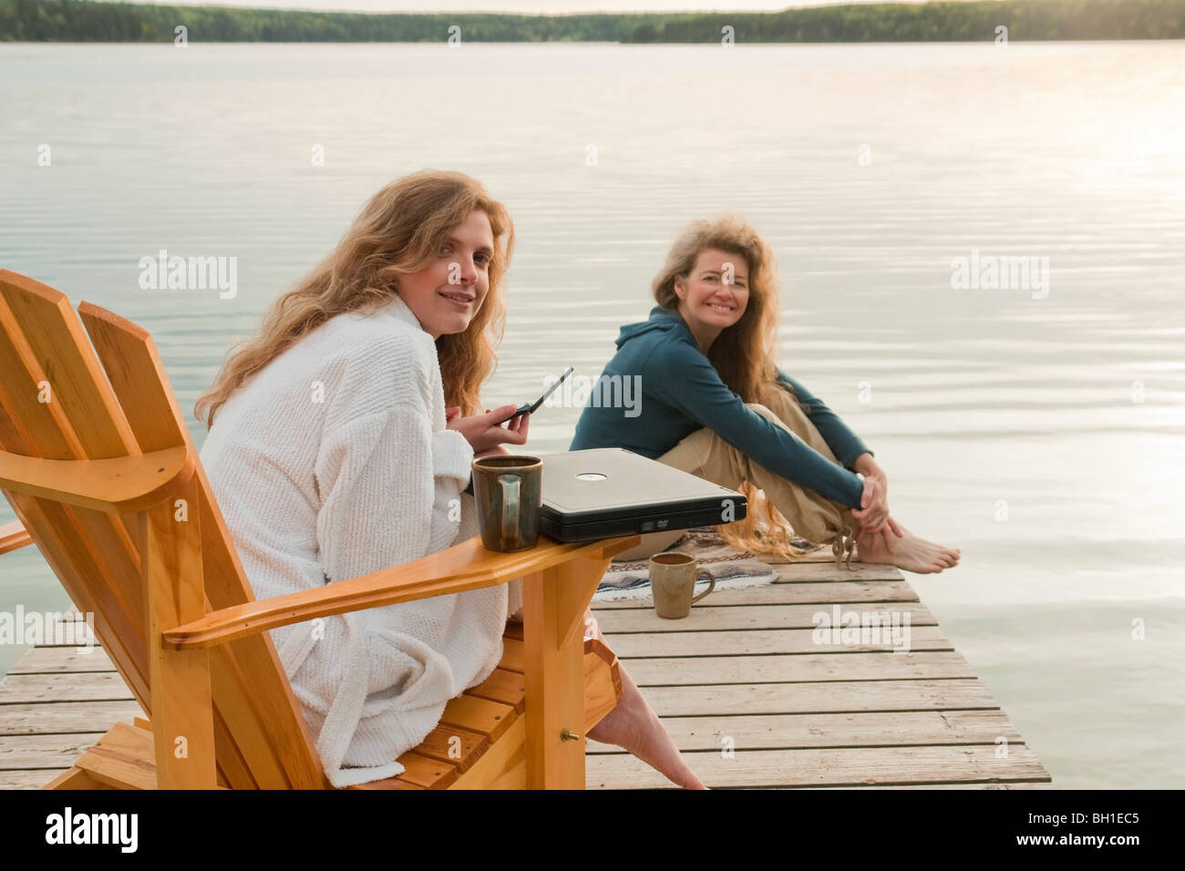 La donna in sedia a sdraio tramite telefono cellulare, seconda donna seduta sul dock, Clear Lake, Manitoba, Canada Foto Stock