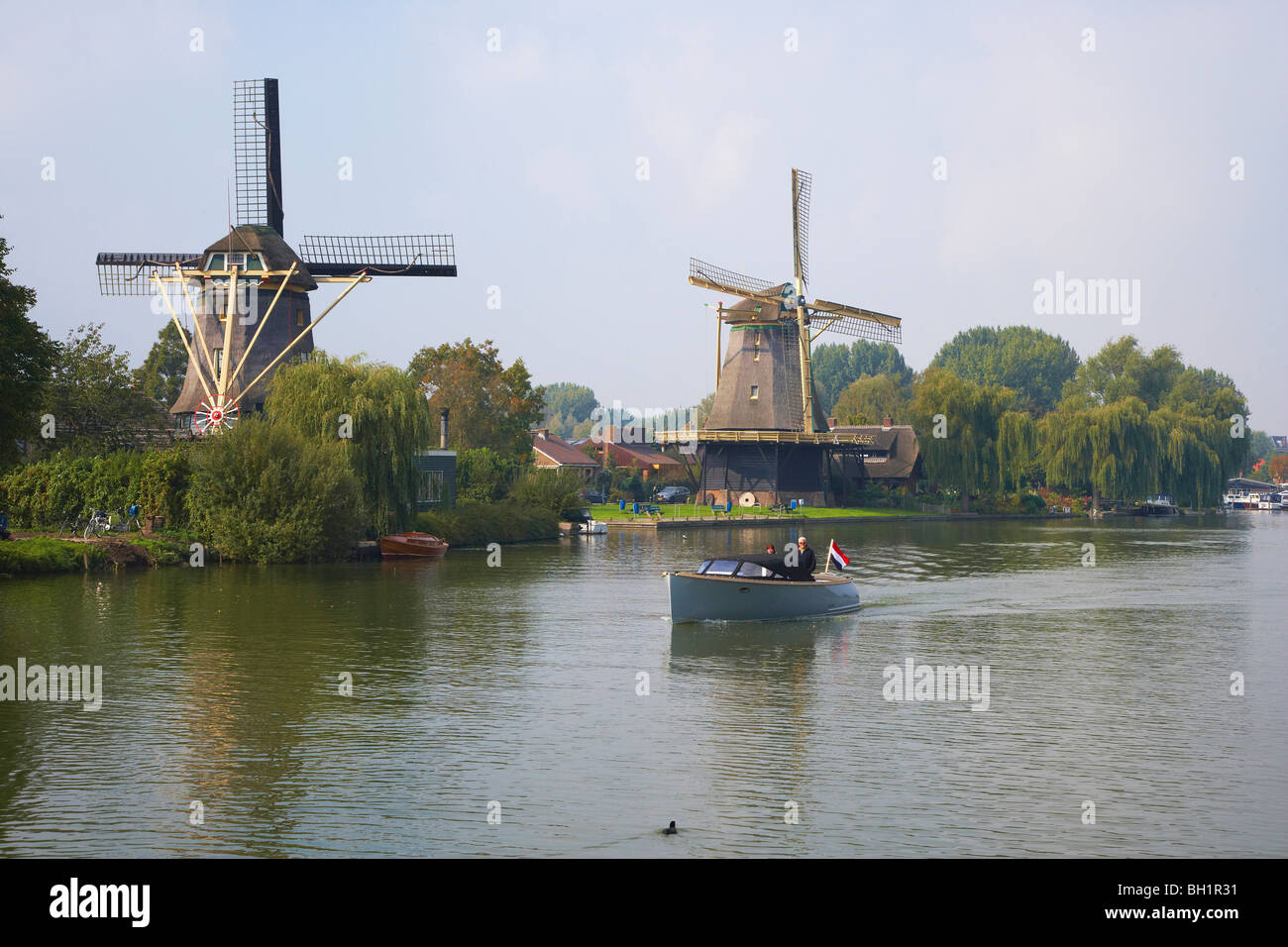 Un motoscafo sul fiume Vecht guida passato due mulini a vento, Weesp, Paesi Bassi, Europa Foto Stock