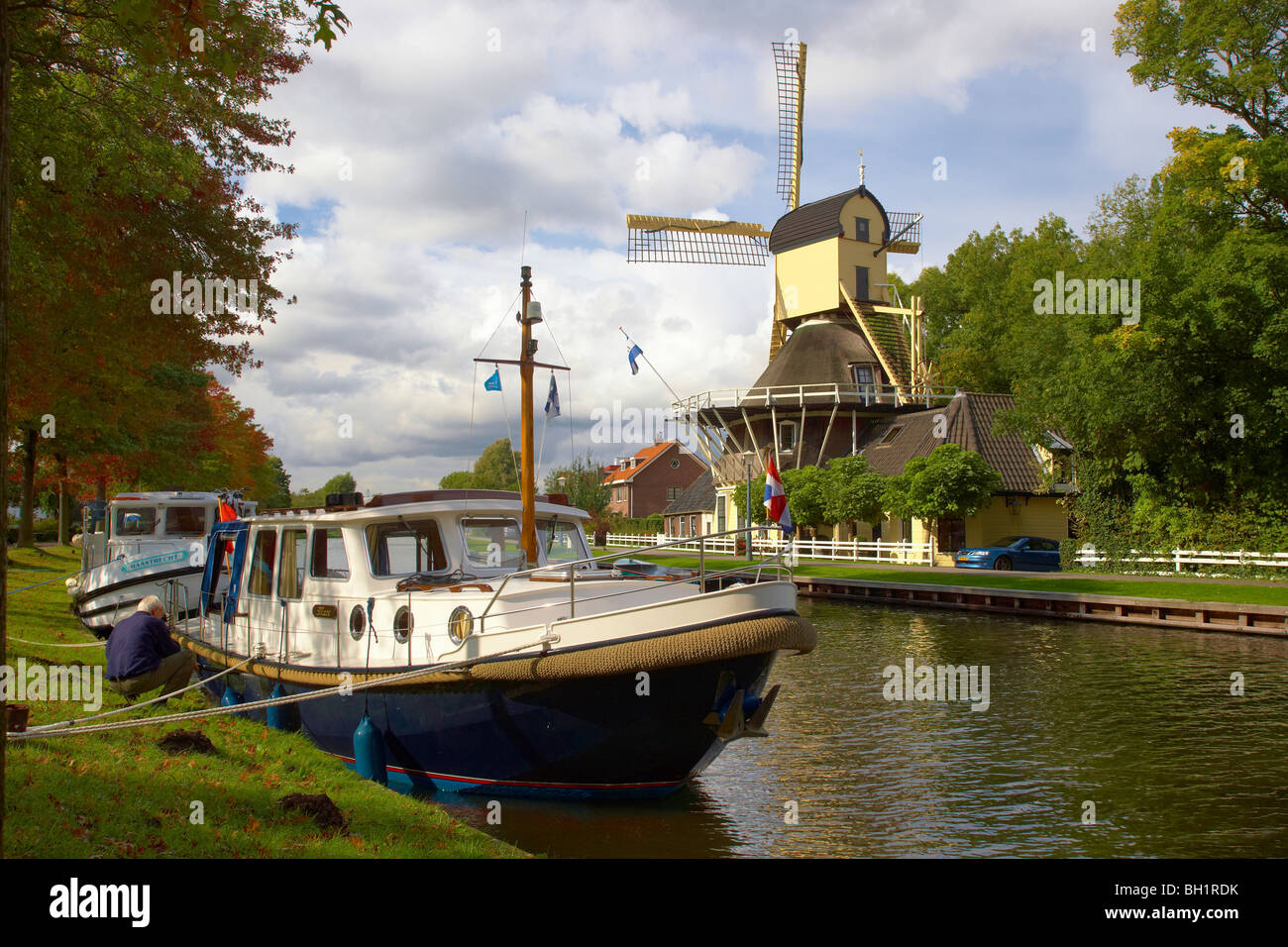 Il mulino a vento e houseboat a teh rive del fiume Smal Weesp sotto il cielo nuvoloso, Weesp, Paesi Bassi, Europa Foto Stock