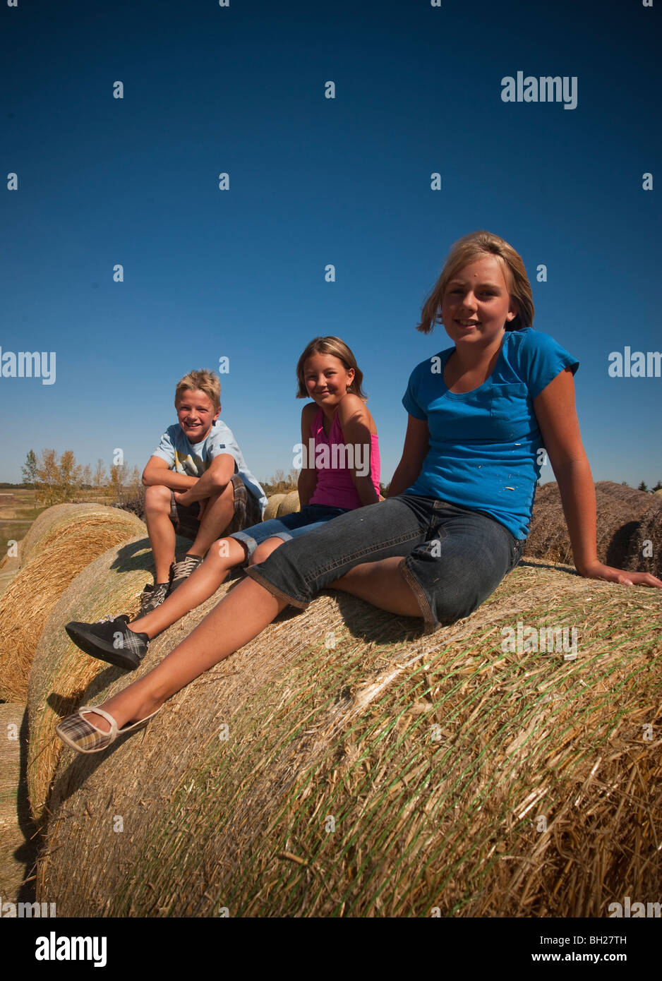 Ragazzo (12) ragazza (10) e una ragazza (12) seduti su balle di paglia; Redvers, Saskatchewan, Canada Foto Stock