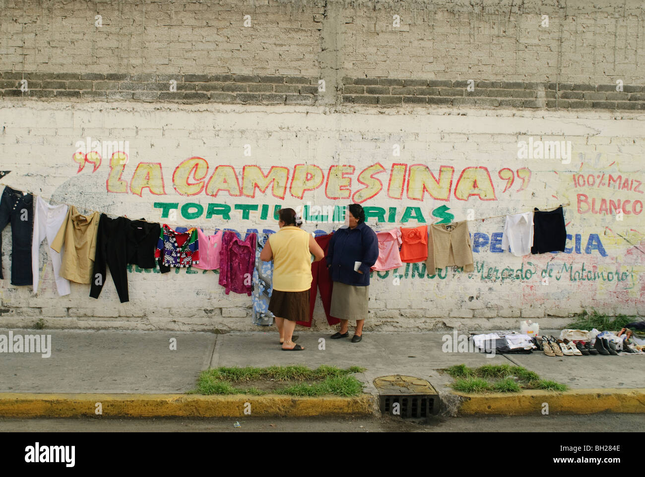 Una donna vende abbigliamento usato appeso a una fune sul lato di un edificio in Ciudad Nezahualcoyotl, Messico. Foto Stock