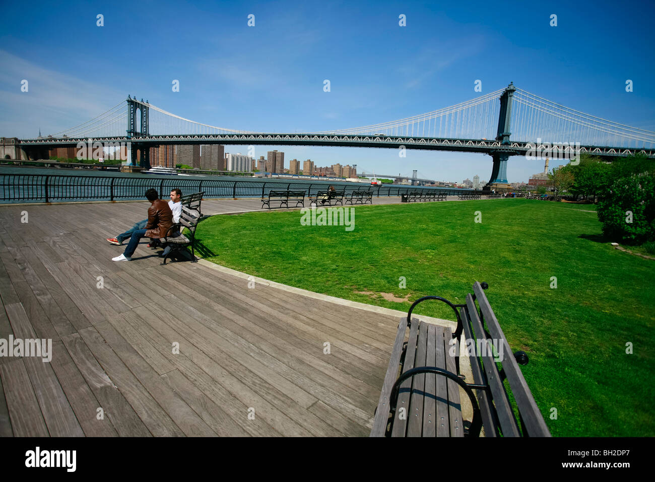 Persone per discutere su un banco vicino alla East River in Dumbo settore con la Manhattan Bridge. Foto Stock