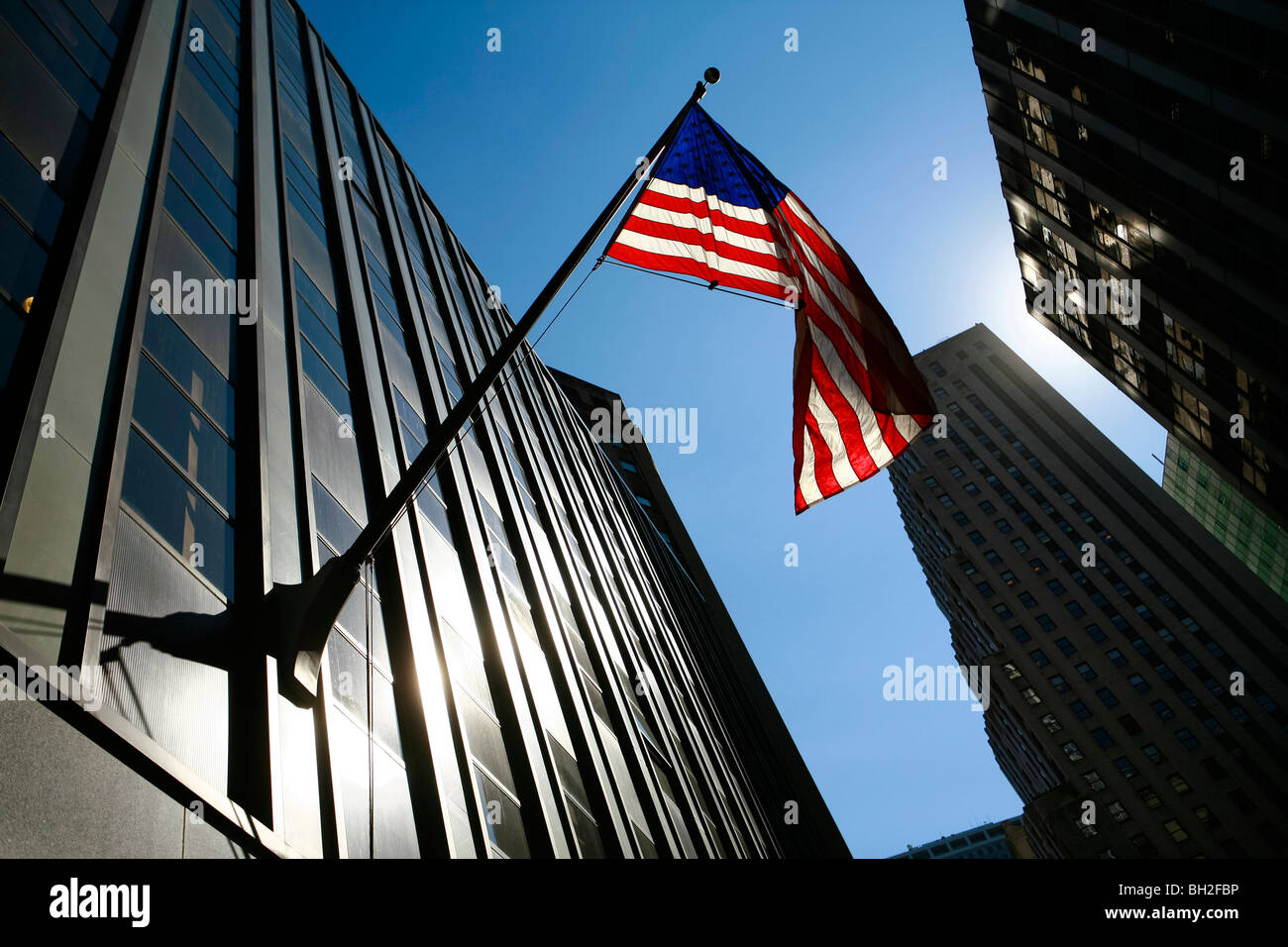 Un soleggiato cielo blu vista di un edificio steelcase facciata vicino alla borsa di New York City e New York dove un enorme bandiera americana è appesa. Foto Stock