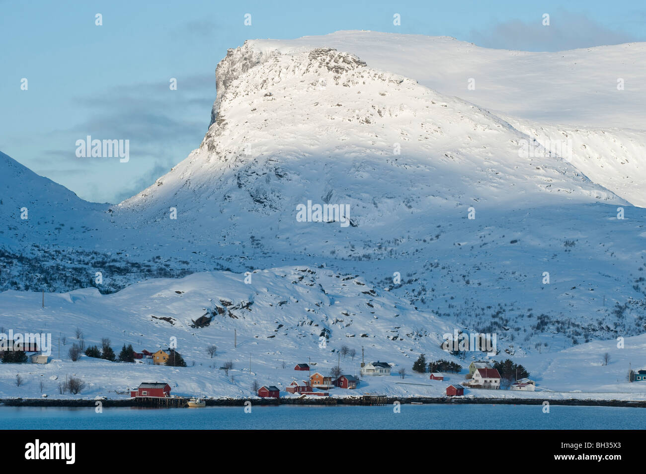 Case, un piccolo villaggio, sotto montagne dalle vette innevate. Paesaggio invernale da Krystad, isole Lofoten, a nord della Norvegia Foto Stock