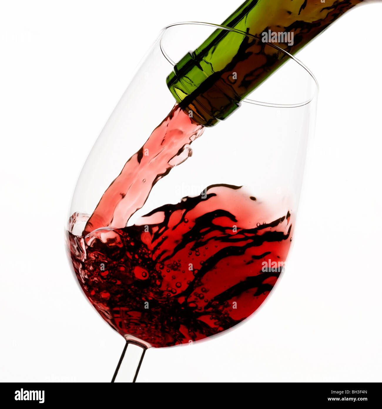 Vino rosso versando in vetro su sfondo bianco Foto Stock
