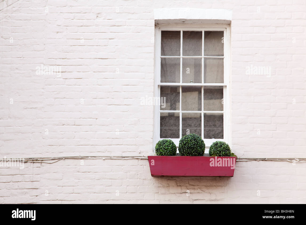 Semplice finestra rossa con copertura sotto le finestre a doppia sporgenza e parete bianca. Arundel, West Sussex, Regno Unito Foto Stock