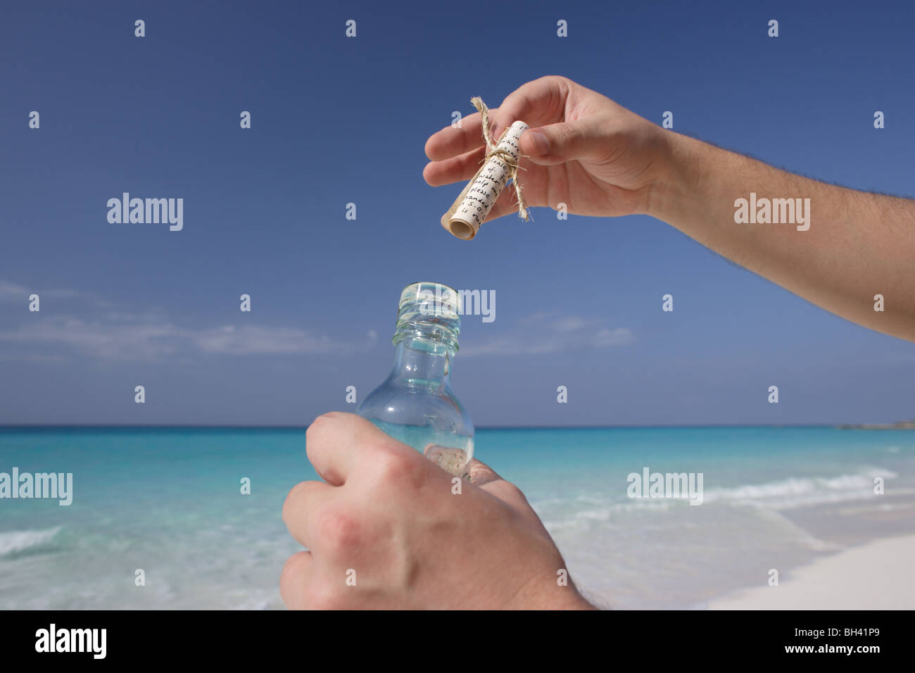 Un uomo con le mani in mano tenendo un messaggio in bottiglia su una deserta spiaggia tropicale Foto Stock