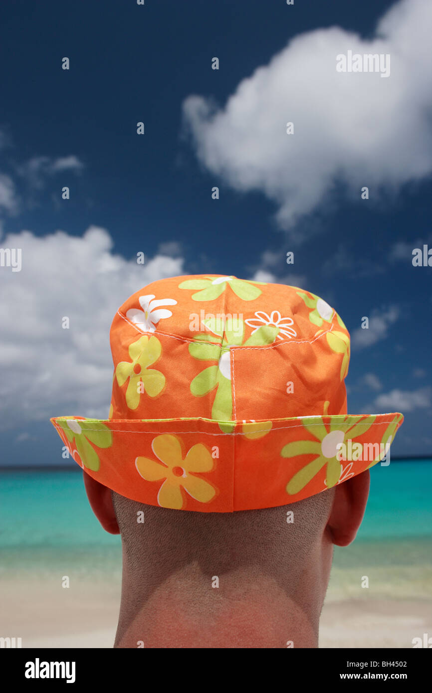 Close up di un uomo che indossa un vivacemente colorato cappello per il sole guardando fuori all'orizzonte su una spiaggia tropicale Foto Stock