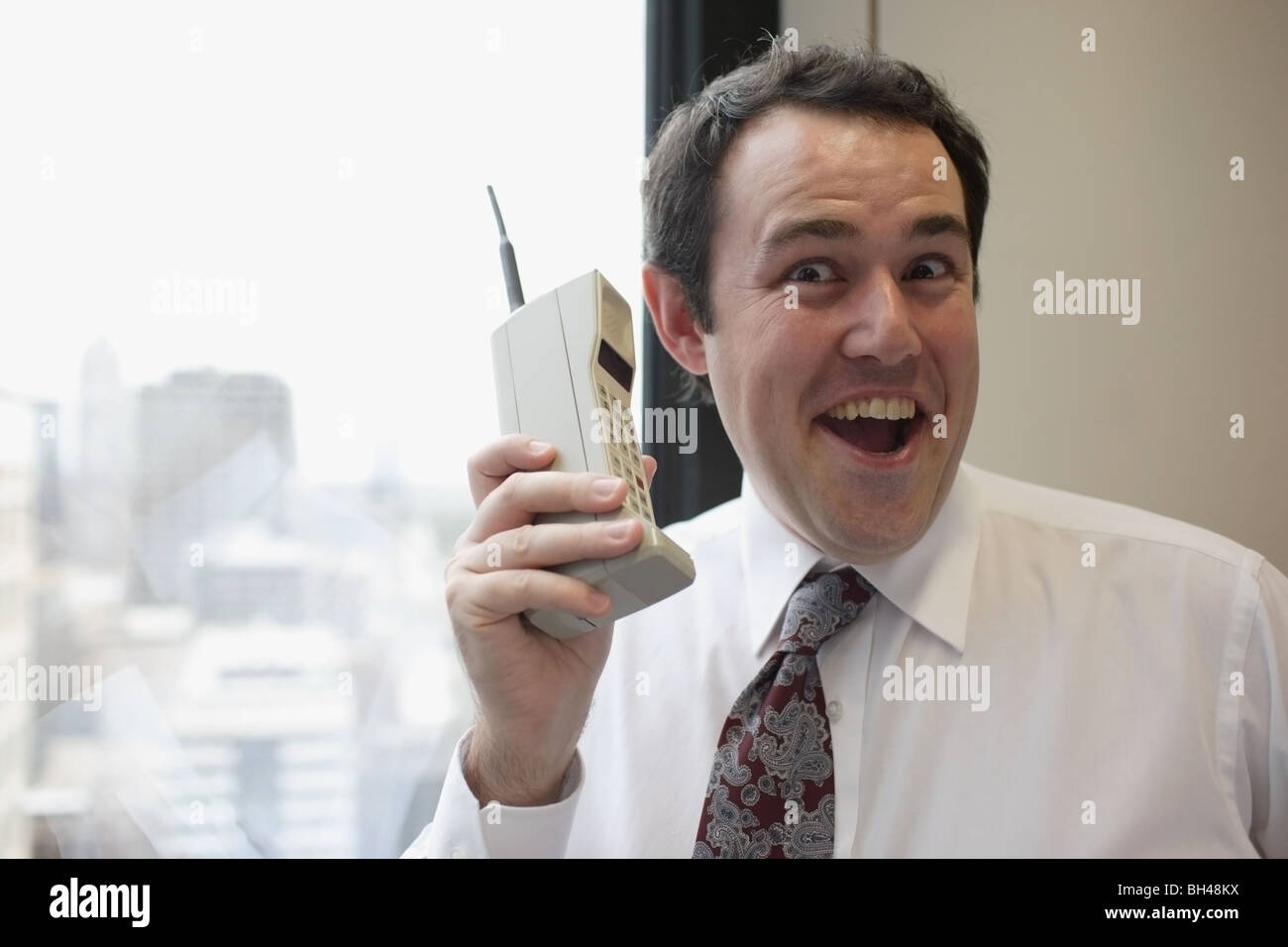 Imprenditore tenendo un vecchio telefono cellulare, ridendo Foto Stock