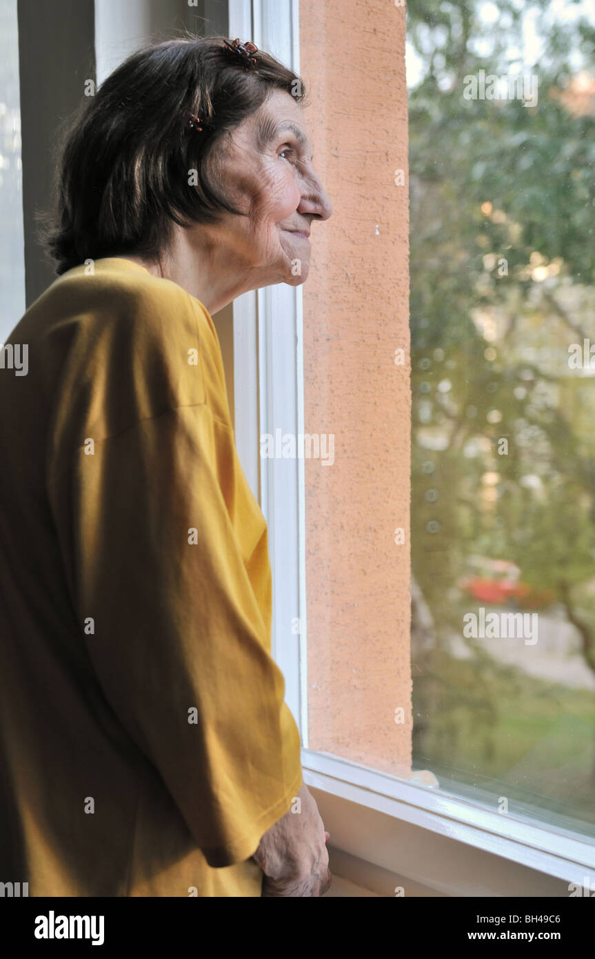 Concetto di solitudine - triste 80s senior donna che guarda attraverso la finestra a casa Foto Stock
