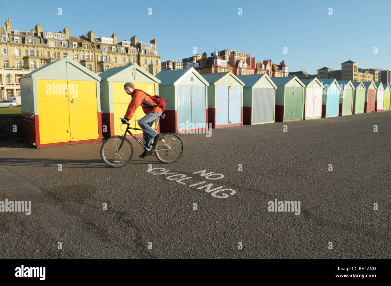 Un ciclista in sella alla sua moto su Hove e Brighton Seafront passato la spiaggia di capanne e un 'no ciclismo 'segno Foto Stock