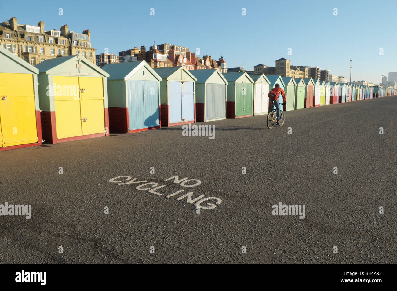 Un ciclista in sella alla sua moto su Hove e Brighton Seafront passato la spiaggia di capanne e un 'no ciclismo 'segno Foto Stock