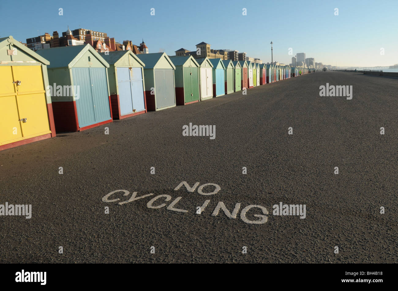 Un ciclista in sella alla sua moto su Hove e Brighton Seafront passato la spiaggia di capanne e un 'no ciclismo 'segno Foto Stock