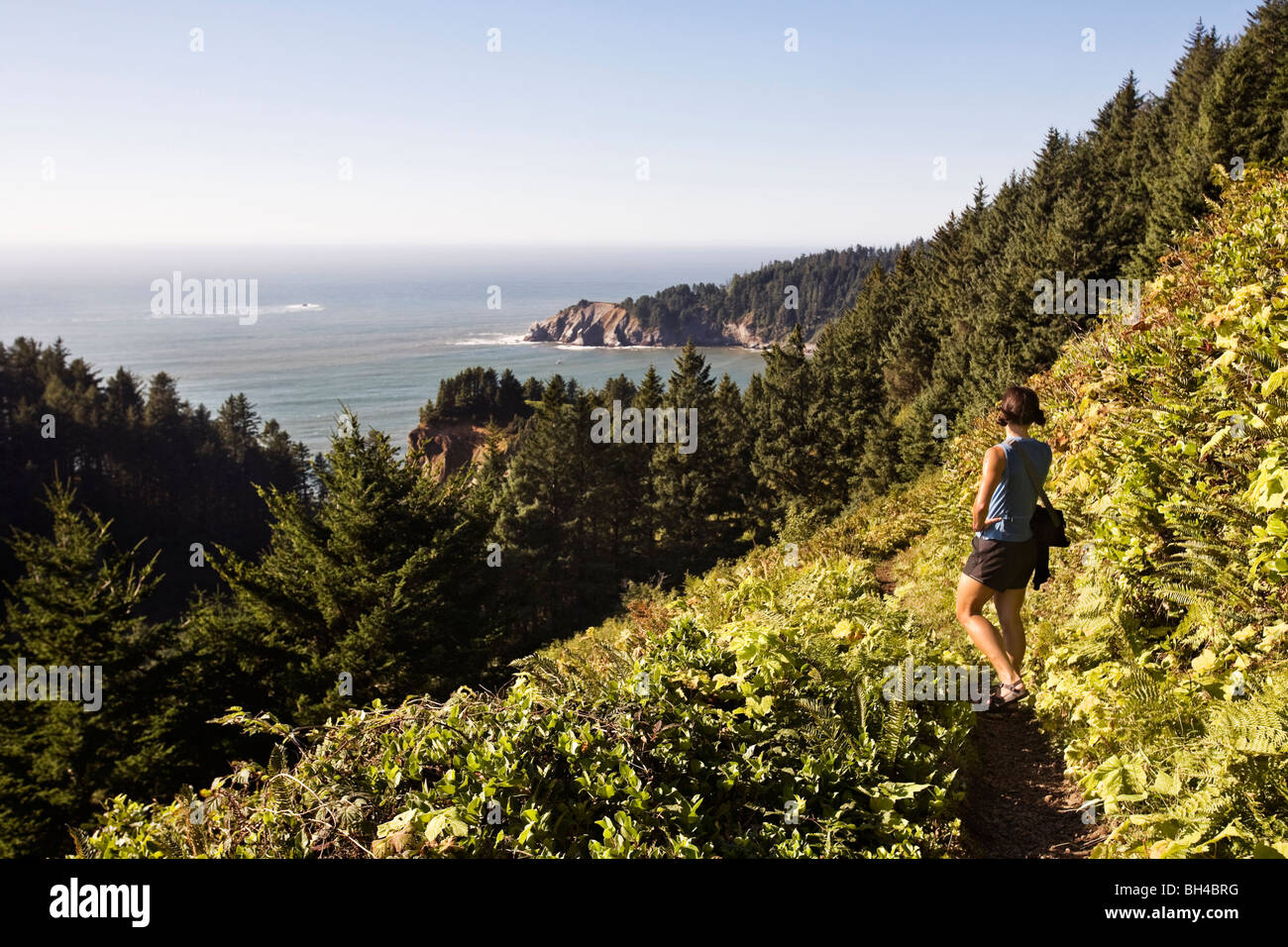 Una donna che indossa abiti estivi Neahkahnie escursioni in montagna, un sentiero costiero in Northwest Oregon e pause per guardare oltre la guarnizione Foto Stock