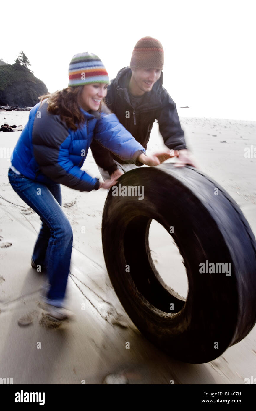 Un uomo e una donna roll un pneumatico vecchio trovato sulla seconda spiaggia sulla Penisola Olimpica a Washington. Foto Stock