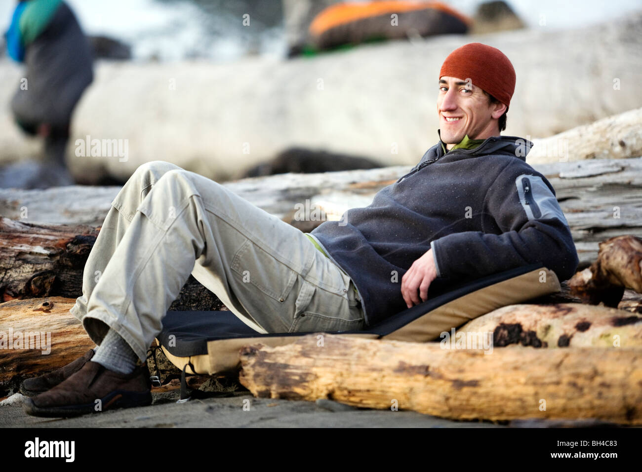Un uomo giace rilassato su una spiaggia con driftwood. Foto Stock