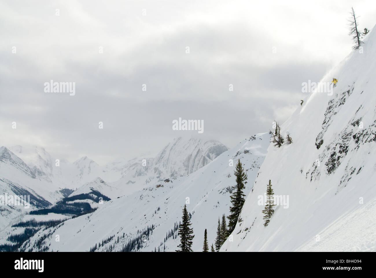 Una donna gli sci una ripida linea con la massiccia cime delle montagne rocciose Canadesi come sfondo. Foto Stock