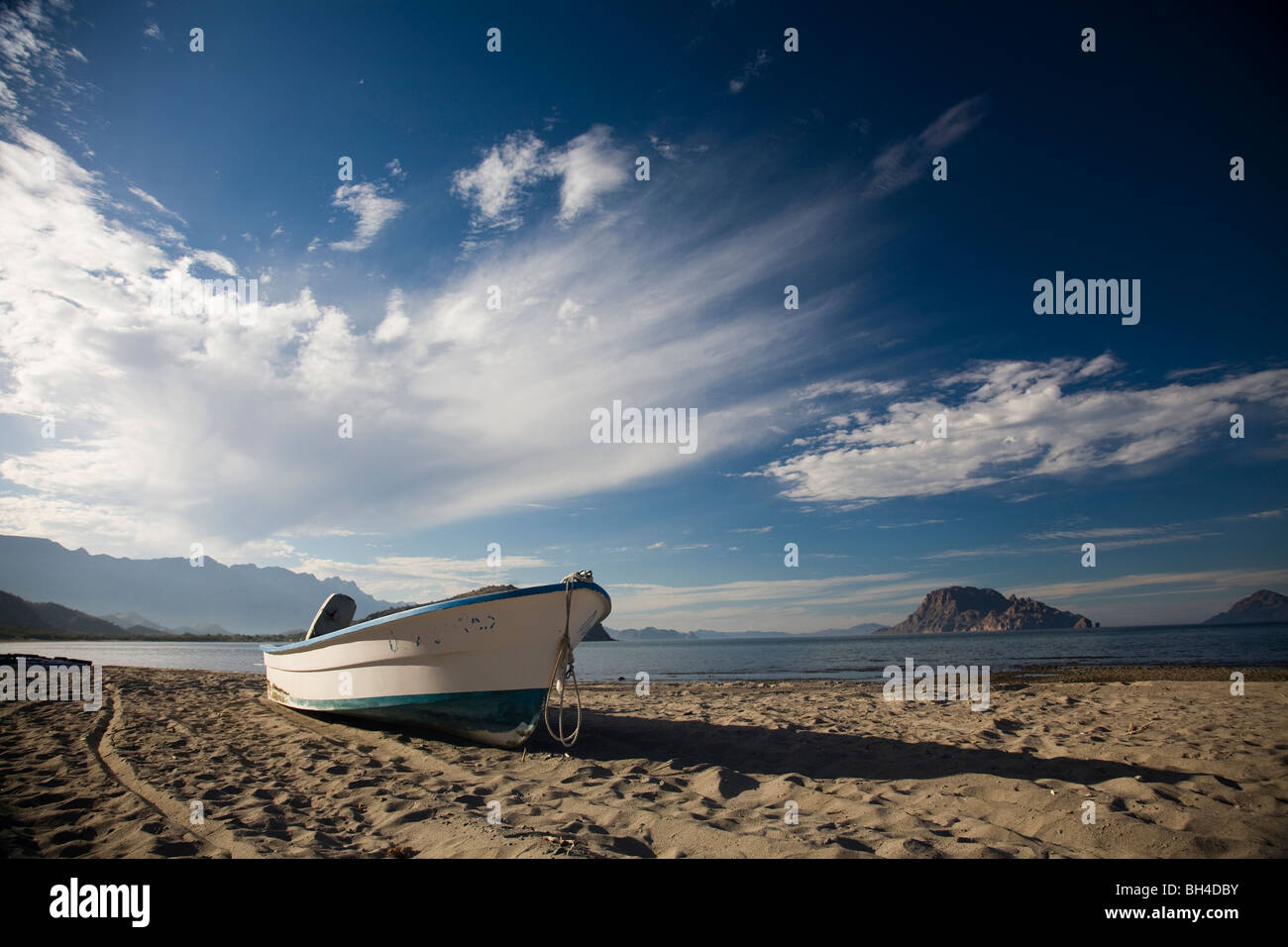 Una barca che si siede sulla sabbia su una spiaggia deserta sotto un poco nuvoloso sky a Loreto, Baja California Sur, Messico. Foto Stock