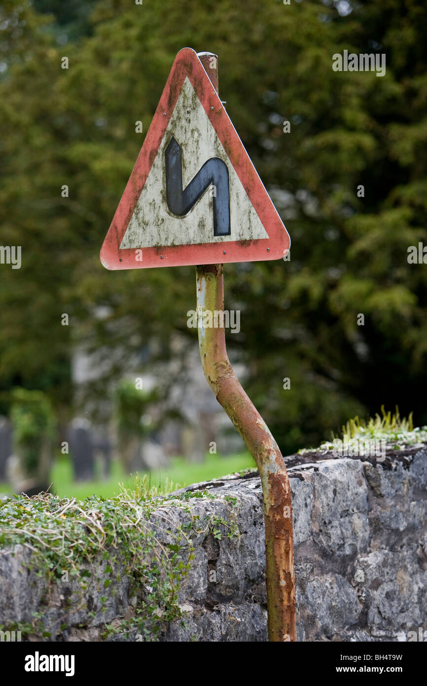 Doppia piega prima a sinistra cartello stradale. Crooked segno su crooked post. Pen-Y-Dyffryn. Il Galles. Regno Unito. Foto Stock