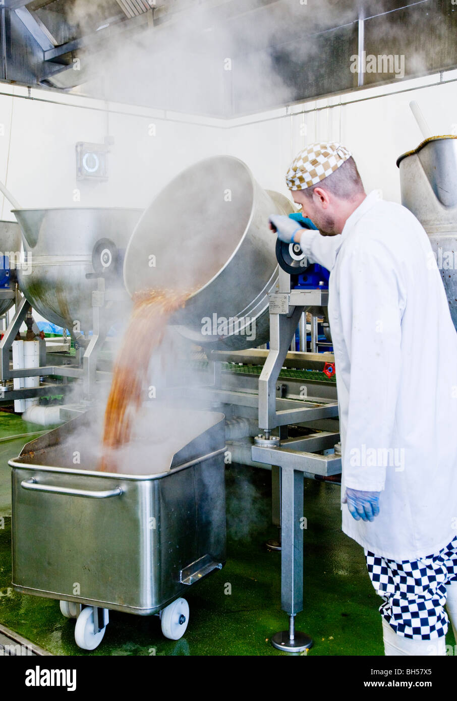 All'interno di un alimento fabbrica di marmellate e sottaceti e condimenti che mostra un lavoratore di sesso maschile lo svuotamento di un calderone di sottaceti in una grande vasca. Foto Stock