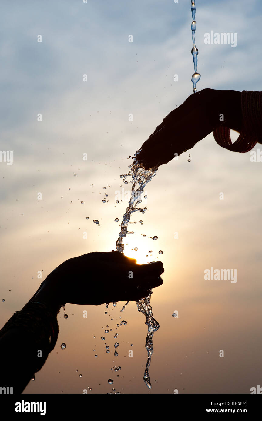 Le mani versando acqua da uno all'altro al tramonto. Silhouette. Andhra Pradesh, India Foto Stock