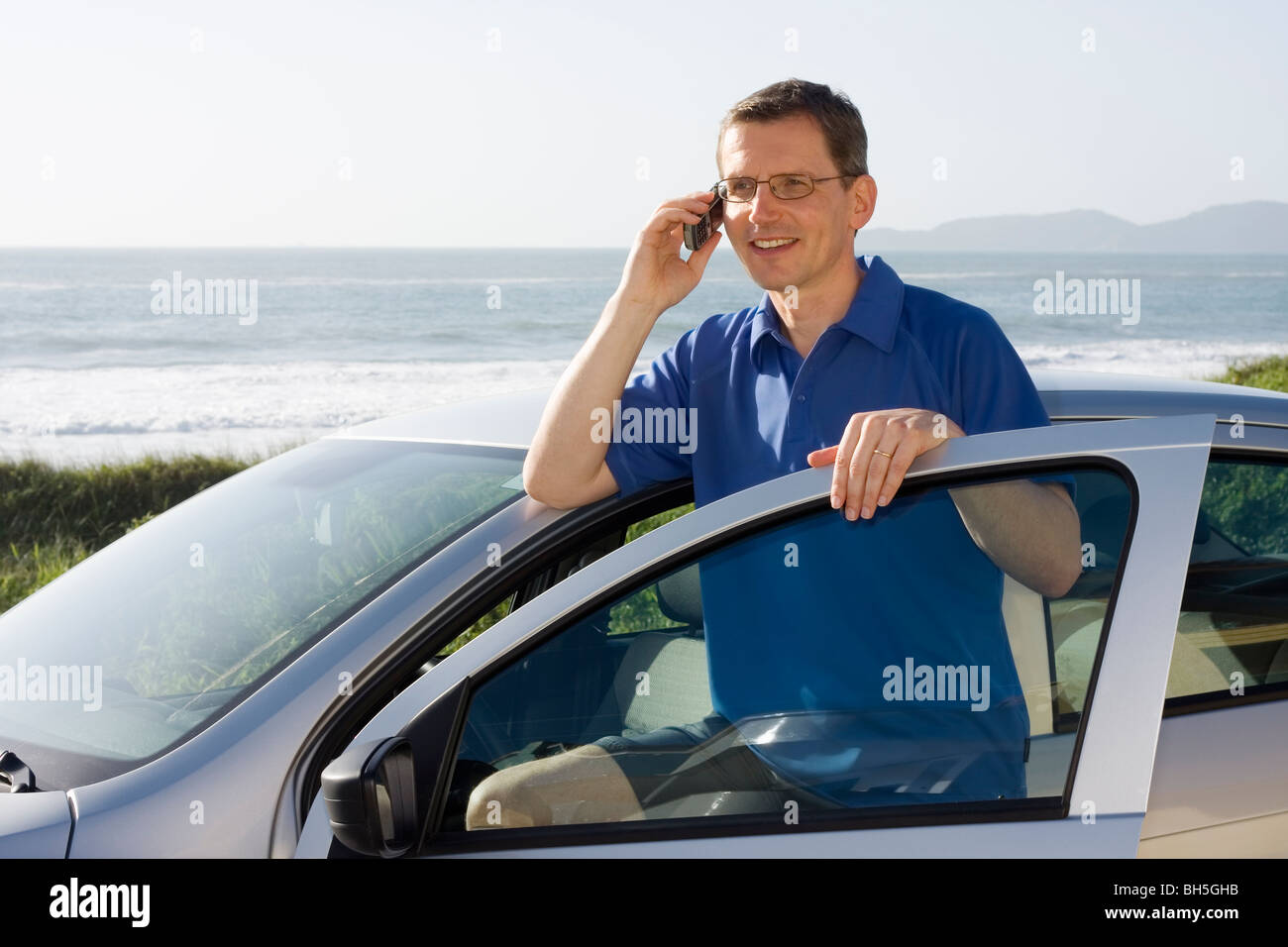 Uomo che parla su telefono cellulare a fianco di una vettura al mare Foto Stock