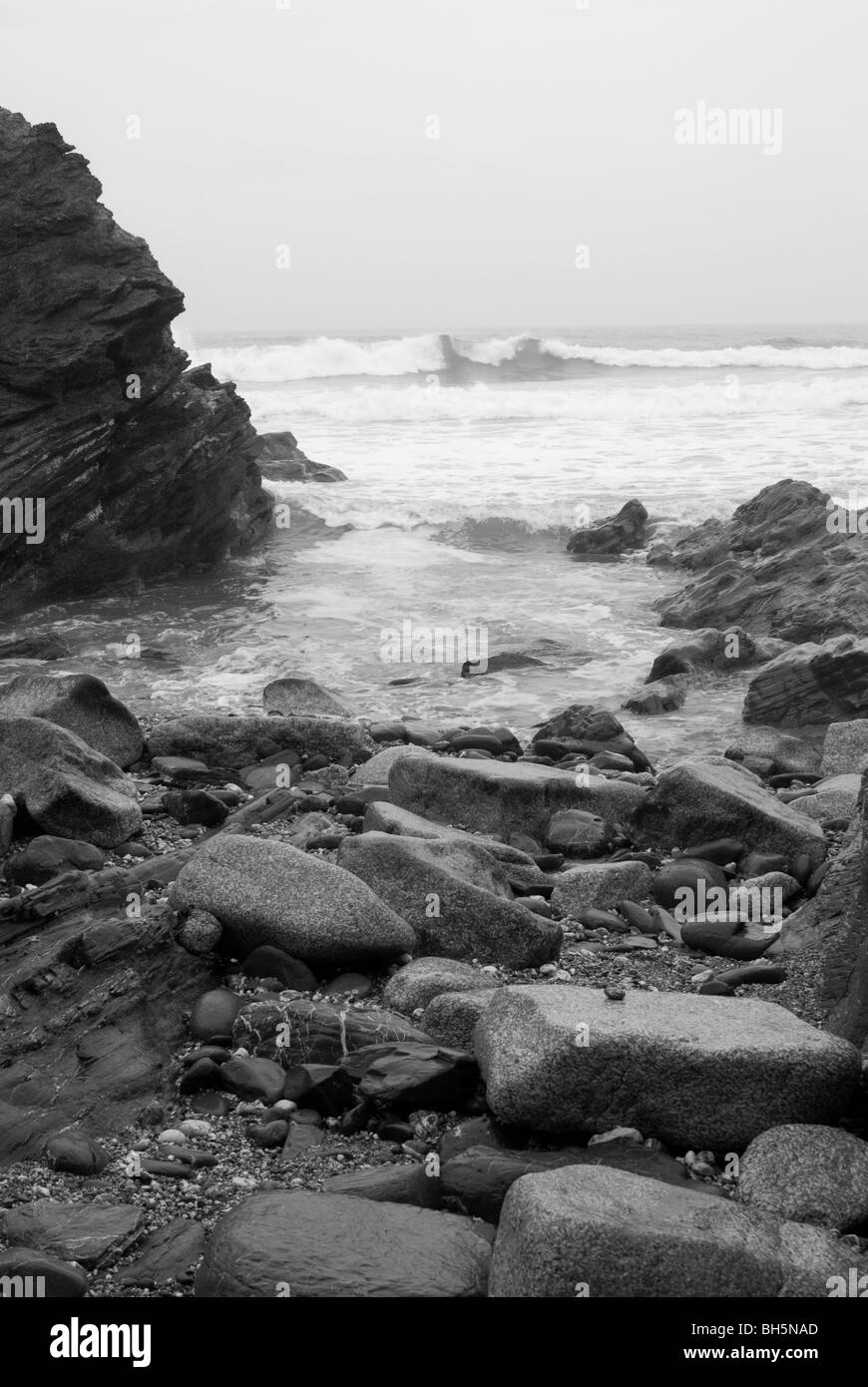 Foreshore roccioso con il surf rompe su una spiaggia della Cornovaglia in bianco e nero Foto Stock