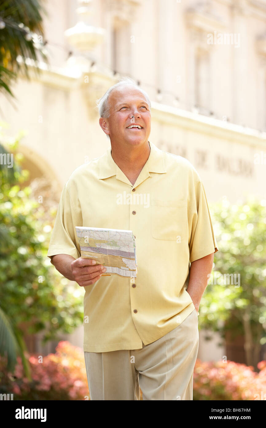 Senior uomo a piedi attraverso una strada di città con mappa Foto Stock