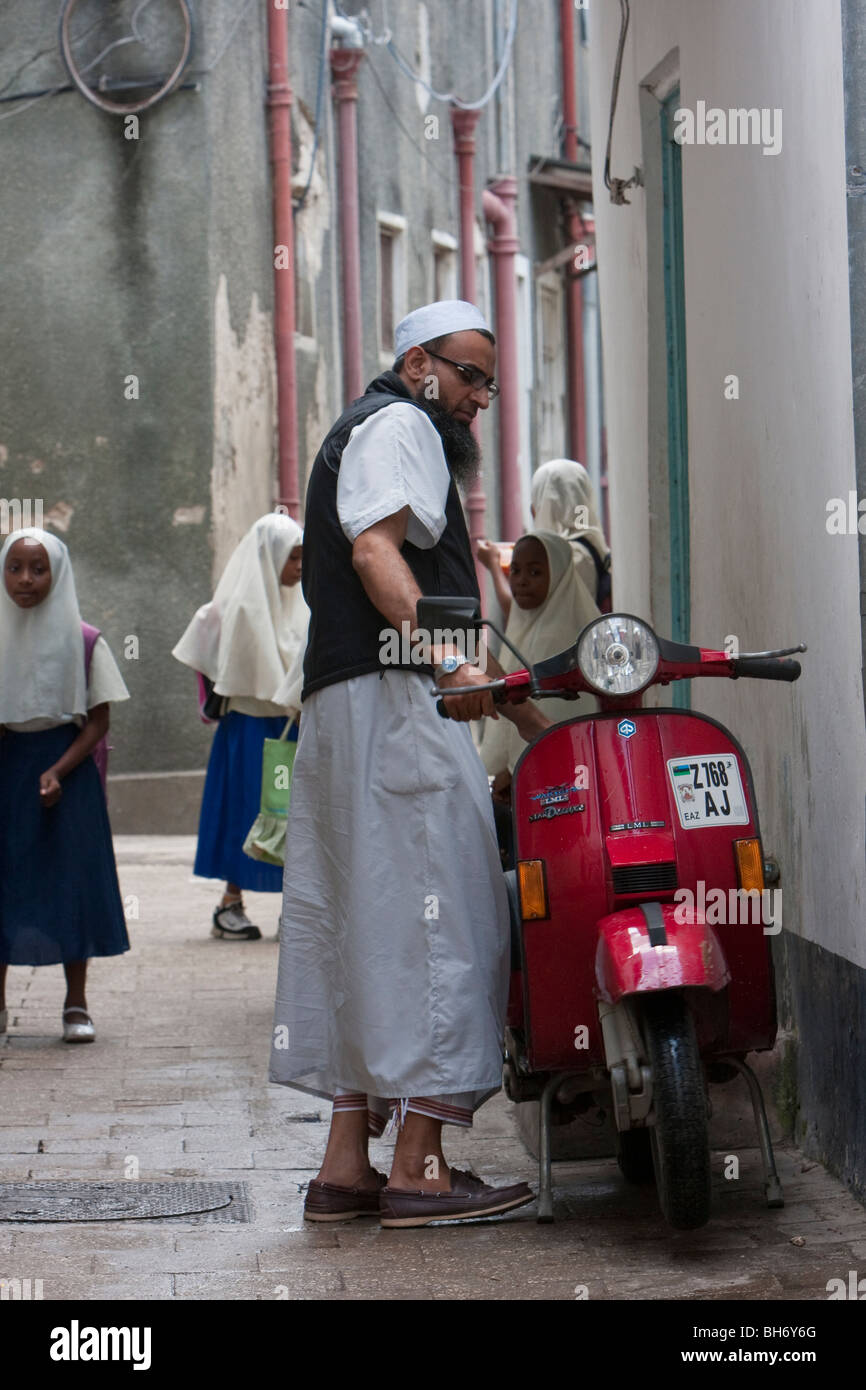 Stone Town, Zanzibar, Tanzania. Zanzibari araba e il suo scooter. Egli indossa una kikoi, un singolo pezzo di stoffa avvolta intorno alla vita. Foto Stock