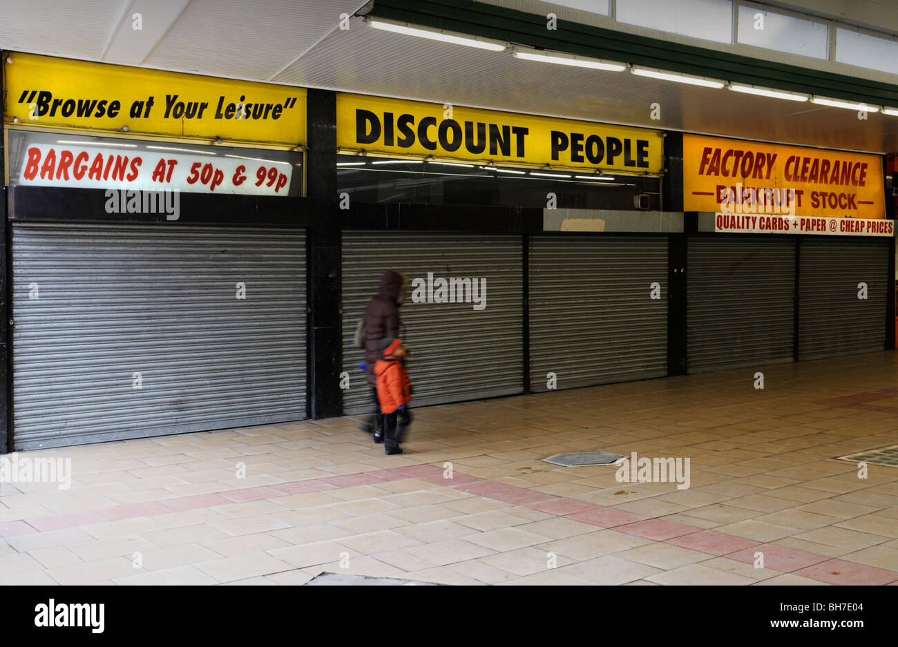 Donna e bambino a piedi passato chiuso negozio di sconto, Croydon, Londra, Inghilterra, Regno Unito. Foto Stock