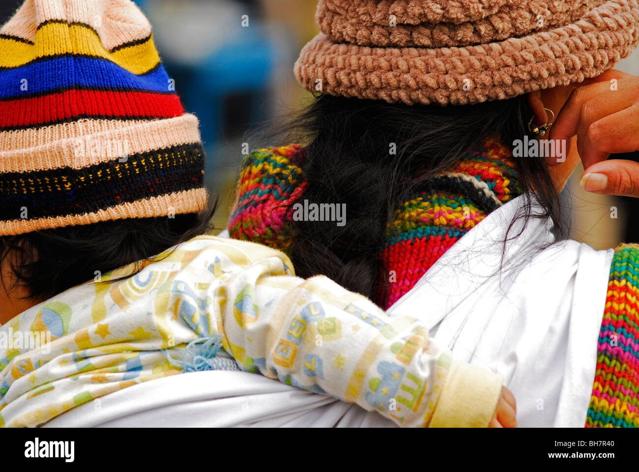 Ecuador, Otavalo, vista posteriore di una madre con un arcobaleno colorato come il cotone Pullover portante una bambina indossa un colorato Foto Stock