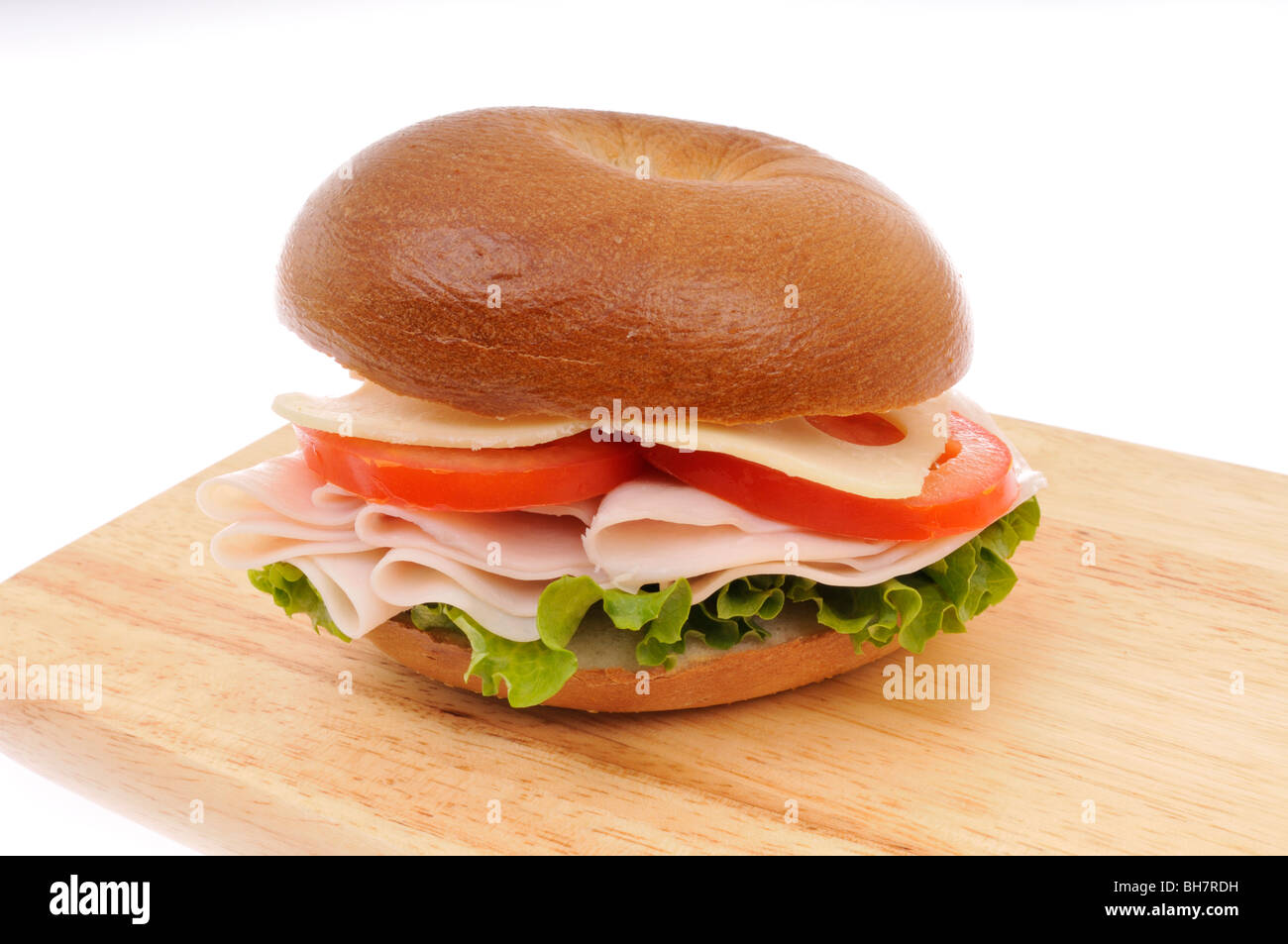 La Turchia, il formaggio svizzero e la lattuga e pomodoro bagel panino su un legno tagliere su sfondo bianco Foto Stock
