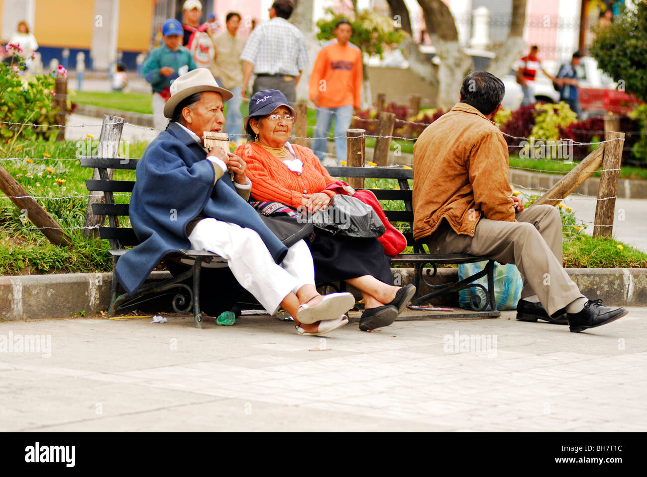 Ecuador, Otavalo, vista di una coppia senior seduto su un banco di lavoro basso nel parco con persone in background Foto Stock