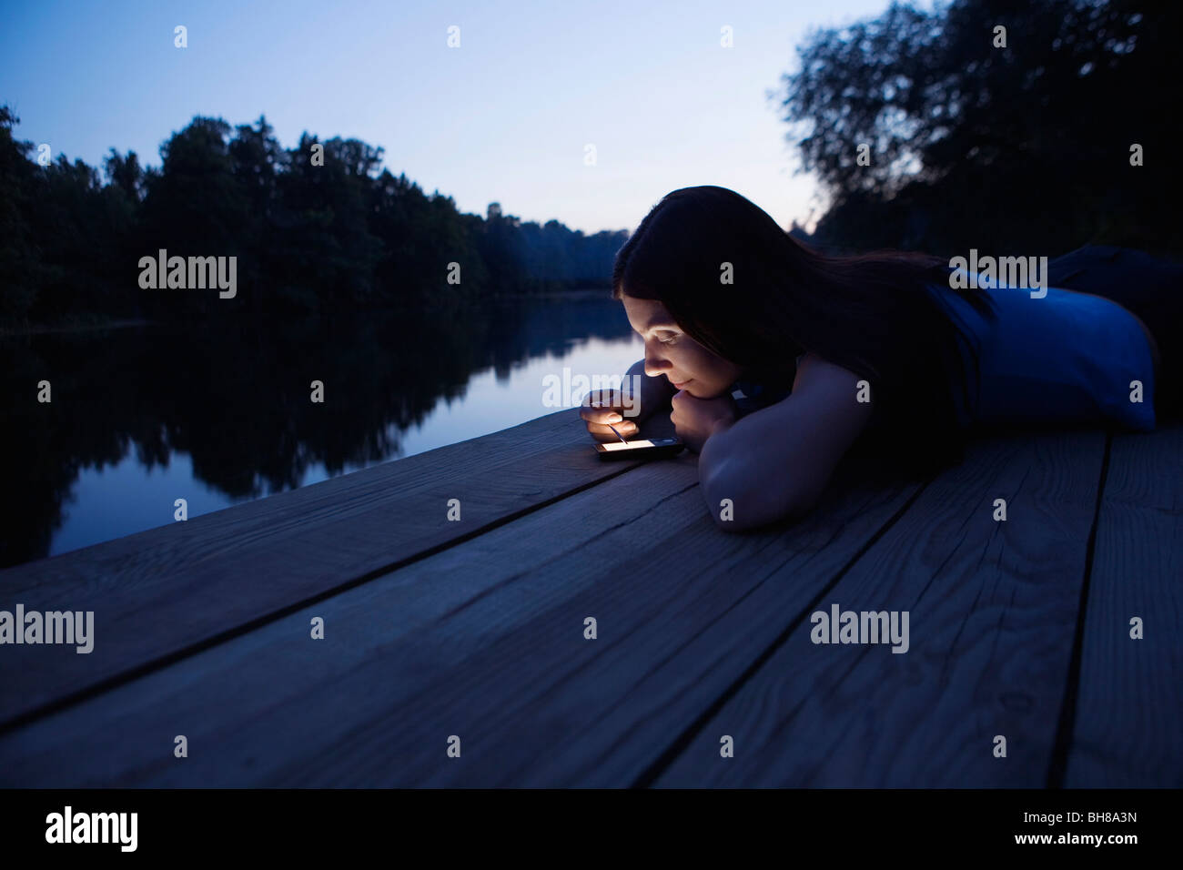 Una donna con un'agenda elettronica mentre giaceva su un molo, crepuscolo Foto Stock